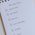 Spiral-Notizblock mit handgeschriebener Selbstfürsorge-Liste, daneben Stift und Eukalyptuszweig