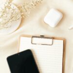 Klemmbrett mit liniertem Papier, Smartphone, Kopfhörer und Stift auf hellem Stoff