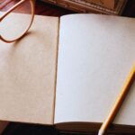Aufgeschlagenes leeres Notizbuch mit Bleistift und Brille auf einem Holztisch