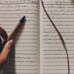 Hand schreibt im Bett mit einem Stift in ein liniertes Notizbuch