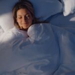 Frau schläft lächelnd in einem Bett mit weißer Bettwäsche