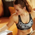 Sportliche Frau in Trainingskleidung sitzt auf dem Sofa und notiert ihren Trainingsplan