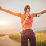Läuferin streckt bei Sonnenaufgang auf einem Feldweg die Arme aus