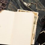 Aufgeschlagenes Reisetagebuch auf Jeansstoff, daneben Fotos, Muschel und Stoffblume
