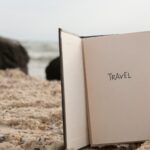 Aufgeschlagenes Buch mit der Aufschrift „Travels“ steht im Sand am Meer