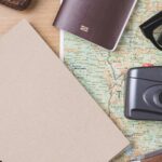 Notizbuch mit Spiralbindung, Kamera, Reisepass, Brille und Taschenmesser auf einer Landkarte