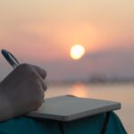 Frau schreibt bei Sonnenuntergang am Meer in ihr Tagebuch