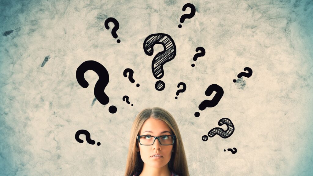 Nachdenkliche junge Frau mit Brille vor einer Wand voller gezeichneter Fragezeichen